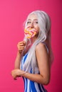 Portrait of a slender woman in a blonde wig posing with a lollipop on a pink background. Cute girl with blue eyes in a Royalty Free Stock Photo