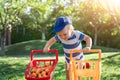 Portrait of small caucasian cute blond toddler boy holding toy shopping cart full of sweet ripe apricots against green Royalty Free Stock Photo