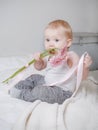 Portrait of 1 small child, blonde girl sitting on the bed in a light top and biting the stems of pink flowers, gerberas Royalty Free Stock Photo