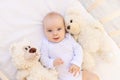 Portrait of a small child a girl 6 months old in a white bodysuit lying on her back in a child`s bed with soft toys bears Royalty Free Stock Photo