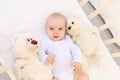 Portrait of a small child a girl 6 months old in a white bodysuit lying on her back in a child`s bed with soft toys bears Royalty Free Stock Photo