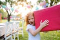 Portrait of small girl with large present box outdoors in garden in summer.