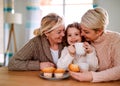 A portrait of small girl with mother and grandmother at the table at home. Royalty Free Stock Photo