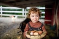 Portrait of small girl standing on farm, holding basket with eggs.