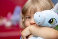 Portrait of a small laughing girl with blonde hair in an embrace with a soft toy on a colored blurred background, close-up, select