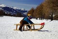 Portrait of small smiling boy sitting on sled on snowy slope on background of sunny mountains Alps and blue sky Royalty Free Stock Photo