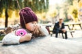 A portrait of a small toddler girl sitting in park in autumn nature.