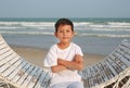 Portrait of smart Asian boy sitting with arms crossed on white bamboo wooden sofa bed with looking camera at the beach Royalty Free Stock Photo