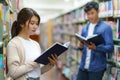 Portrait of Smart Asian man and woman university student reading book between bookshelves in campus library with copyspace Royalty Free Stock Photo
