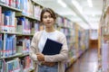 Portrait of Smart Asian woman university student reading book and looking at camera between bookshelves in campus library with Royalty Free Stock Photo