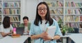 Portrait of smart beautiful young asian girl in glasses holding book in library bookshelf background looking at the Royalty Free Stock Photo