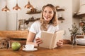 Portrait of smart blond woman reading book and drinking coffee while sitting in cozy cafe indoor Royalty Free Stock Photo