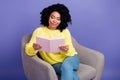 Portrait of smart clever erudite woman with afro hair wear knit sweater sit on armchair read book isolated on violet