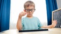 Portrait of smart cute boy wearing glasses playing and studying on tablet computer. CHild using gadget for doing Royalty Free Stock Photo