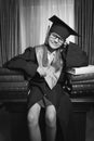 Portrait of smart girl in graduation cap posing on table at libr Royalty Free Stock Photo