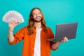 Portrait of smart good mood man with long hairstyle dressed orange shirt hold bunch of dollars laptop isolated on teal Royalty Free Stock Photo