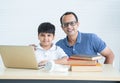 Portrait of smart indian family, child son with father smiling, looking at camera together while doing homework, using laptop Royalty Free Stock Photo