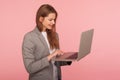 Portrait of smart office employee typing on laptop, elegant positive businesswoman in suit jacket using computer