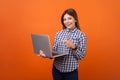 Portrait of smart positive woman with brown hair in checkered casual shirt and denim standing pointing at laptop in her hands,