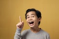 Portrait of smart young Asian boy wearing grey shirt, looking and pointing up, smiling for having good idea gesture Royalty Free Stock Photo