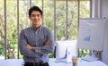 Portrait of smart young asian businessman looking to camera in the office room with computer and meeting board with bar chart. Royalty Free Stock Photo