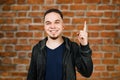 Portrait of smiles adult man on brick wall background. Caucasian man with beard showing pointing finger up Royalty Free Stock Photo