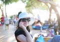 Smiling cute girl wearing sunglasses and a white hat surrounded with people blurred in the background