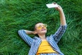 Portrait of smiley young short hair woman in casual blue striped suit, yellow shirt, glasses lying down on green grass holding her Royalty Free Stock Photo