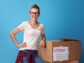 Smiling active woman standing next to cardboard boxes on blue Royalty Free Stock Photo