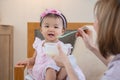 Portrait of smiling adorable Asian baby eating food from spoon, mother feeding little daughter puree or solid foods, toddler Royalty Free Stock Photo