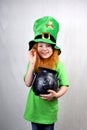 Portrait of smiling adorable girl with decorative red beard, green clover leaf on her cheek and leprechaun hat, dressed in green,