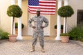 Portrait of smiling african american army man standing with hand on hip against flag on house