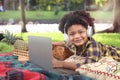 Portrait smiling African American boy with curly hair wear headphones, using laptop computer, lying on green grass at park, kid go Royalty Free Stock Photo