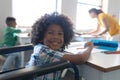 Portrait of smiling african american elementary boy sitting on wheelchair at desk in classroom Royalty Free Stock Photo