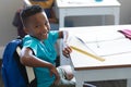 Portrait of smiling african american elementary schoolboy sitting on chair at desk in classroom