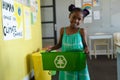 Portrait of smiling african american elementary schoolgirl holding recycle container in school