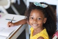 Portrait of smiling african american elementary schoolgirl writing on book at desk in classroom Royalty Free Stock Photo