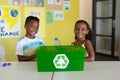Portrait of smiling african american elementary students with recycling container at desk in school Royalty Free Stock Photo