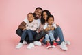 Portrait of smiling african american family of four sitting on floor over pink studio background Royalty Free Stock Photo