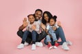 Portrait of smiling african american family of four sitting on floor over pink studio background Royalty Free Stock Photo