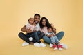 Portrait of smiling african american family of four sitting on floor over yellow studio background Royalty Free Stock Photo