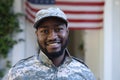 Portrait of smiling african american male soldier standing in front of american flag outside home Royalty Free Stock Photo