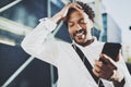 Portrait of Smiling African American man in headphones standidng in sunny street enjoying to music on his smart phone Royalty Free Stock Photo