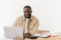 Portrait of smiling african american man looking at camera while sitting at table in home office and working on laptop Royalty Free Stock Photo