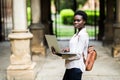 Portrait of smiling African american student doing homework outdoors using laptop for research. Positive dark skinned girl styling