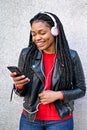 Portrait of a smiling African-American woman with a cell phone is chatting or listening to music on the streets of the city. The Royalty Free Stock Photo