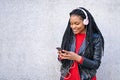 Portrait of a smiling African-American woman with a cell phone is chatting or listening to music on the streets of the city. The Royalty Free Stock Photo