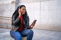 Portrait of a smiling African-American woman with a cell phone is chatting or listening to music on the streets of the city. The Royalty Free Stock Photo