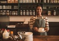 Smiling African barista standing in her cafe holding a cappuccino Royalty Free Stock Photo