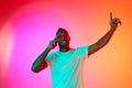 Portrait of smiling african man looking at camera and moves his hands to the side over gradient colorful background in Royalty Free Stock Photo